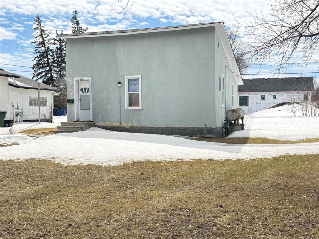 A small house with a grey exterior and a white door stands in a snowy landscape.