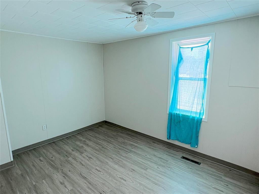 A room with a ceiling fan and a window with a blue curtain.