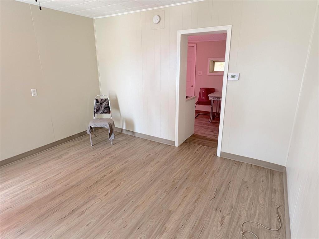 A room with a wooden floor and a white wall with a doorway leading to another room.