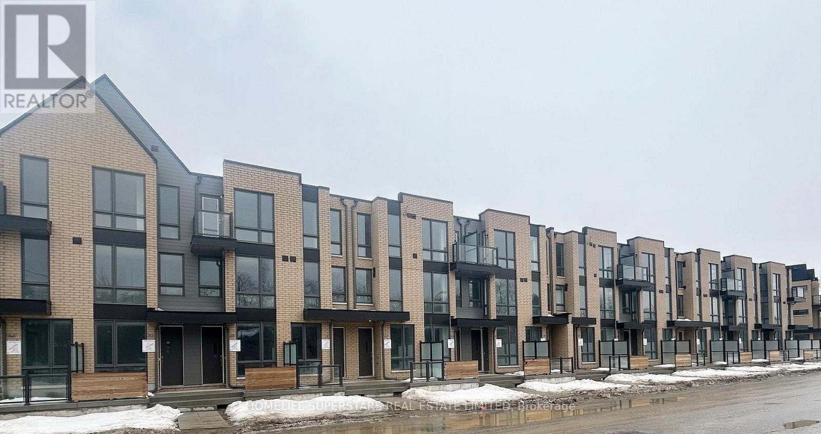 A row of modern townhouses with a realtor logo in the corner.