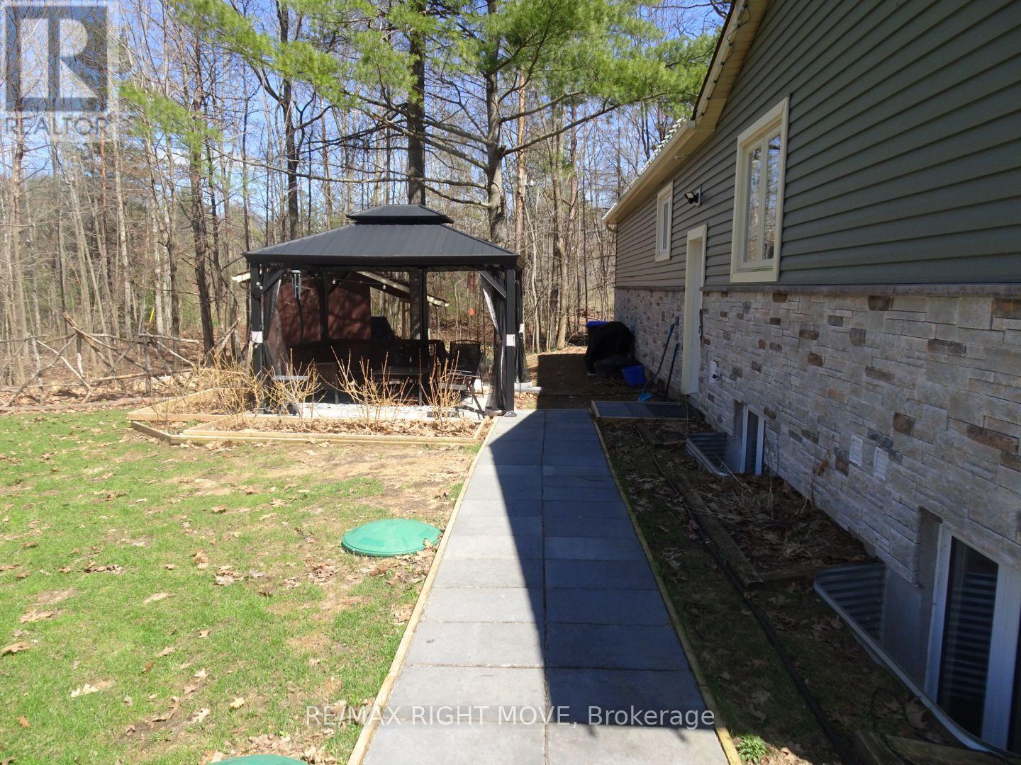 A gazebo is in a yard next to a house.
