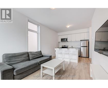 A grey couch sits in a white living room with a kitchen area in the background.