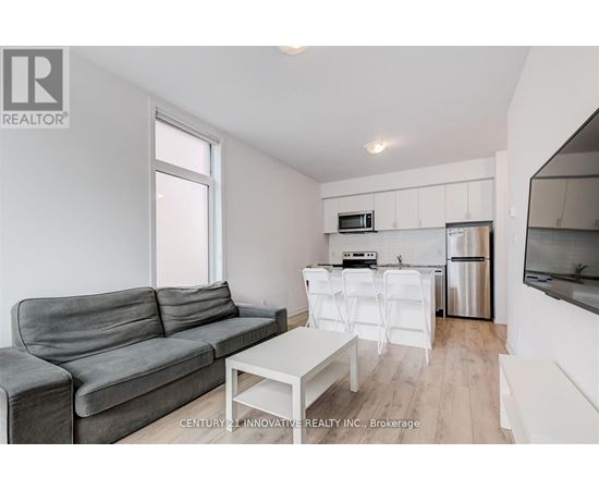 A grey couch sits in a white living room with a kitchen area in the background.