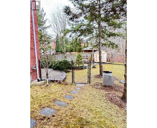 A backyard with a fence, a trash can, and a pathway.