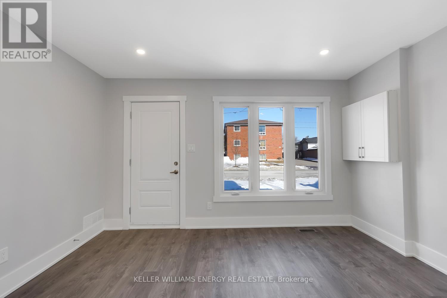 A room with a door and a window showing a building outside.