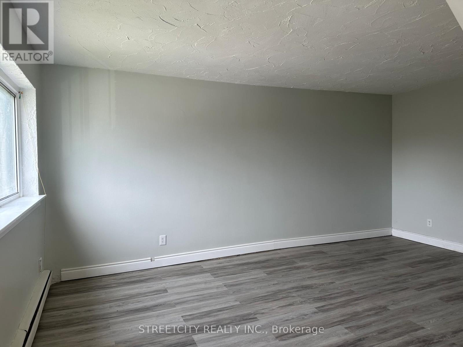 A room with a wooden floor and a window on the left side.