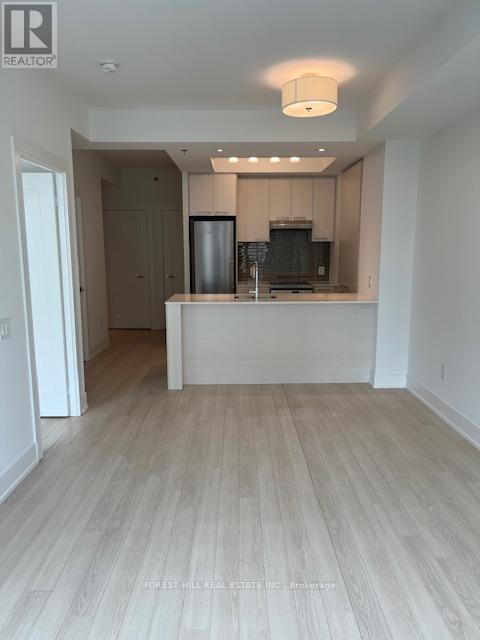 A well-lit, empty kitchen and living room with wooden flooring.