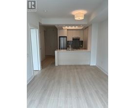 A well-lit, empty kitchen and living room with wooden flooring.