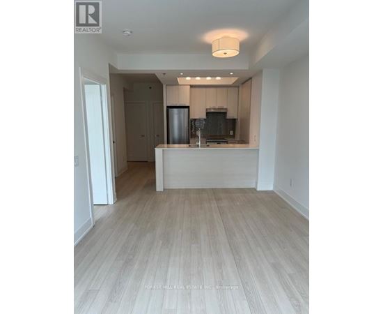 A well-lit, empty kitchen and living room with wooden flooring.