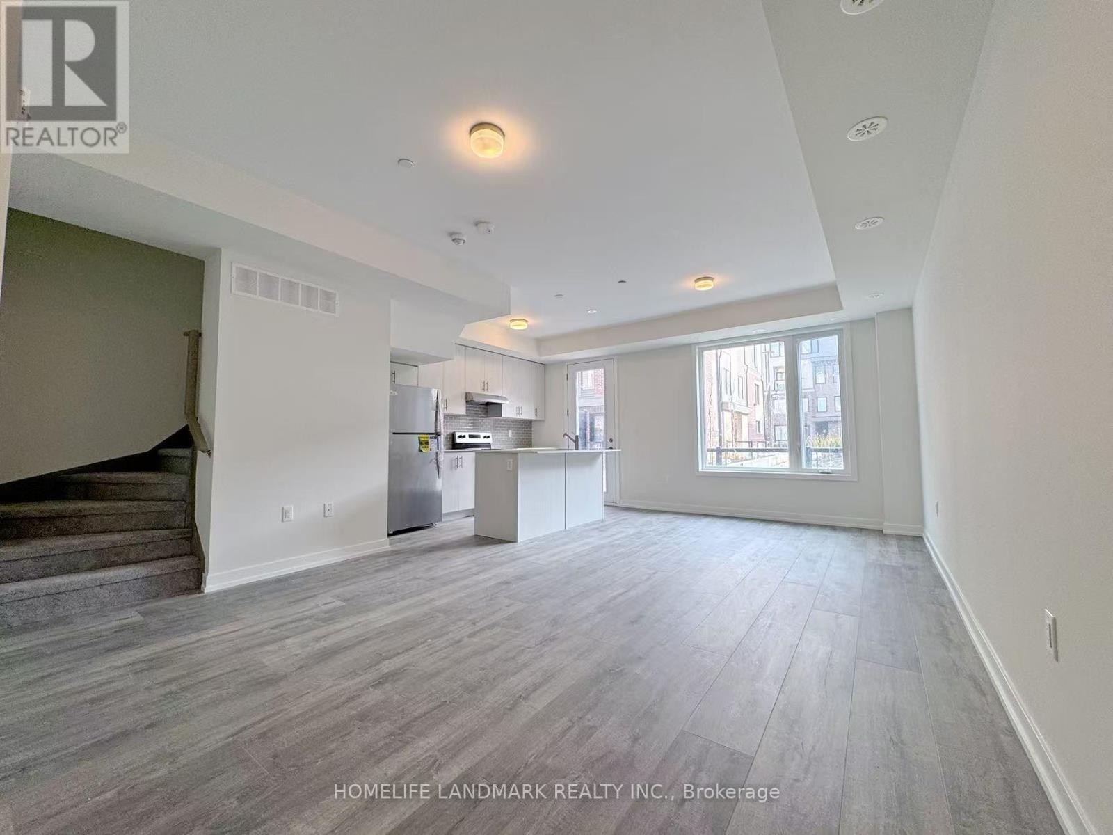 A spacious living room with wood flooring and a staircase on the left side.