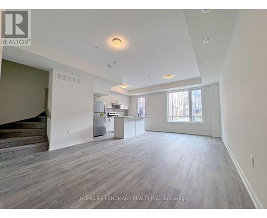 A spacious living room with wood flooring and a staircase on the left side.