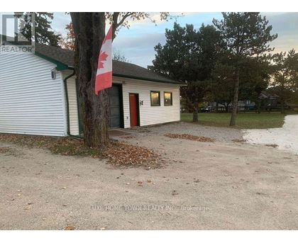 A small white building with a red door and a Canadian flag on a tree.