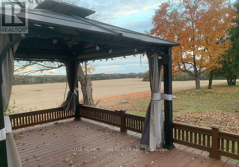 A gazebo with a black roof and grey curtains is situated on a wooden deck.