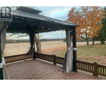 A gazebo with a black roof and grey curtains is situated on a wooden deck.