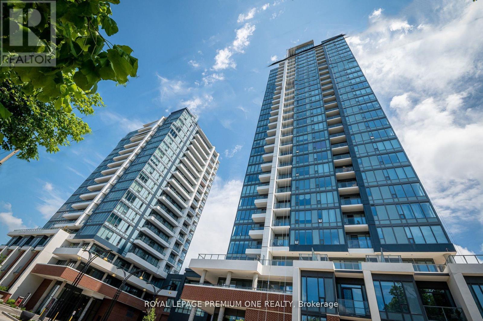 Two modern high-rise buildings with glass windows and balconies are under a blue sky with clouds.