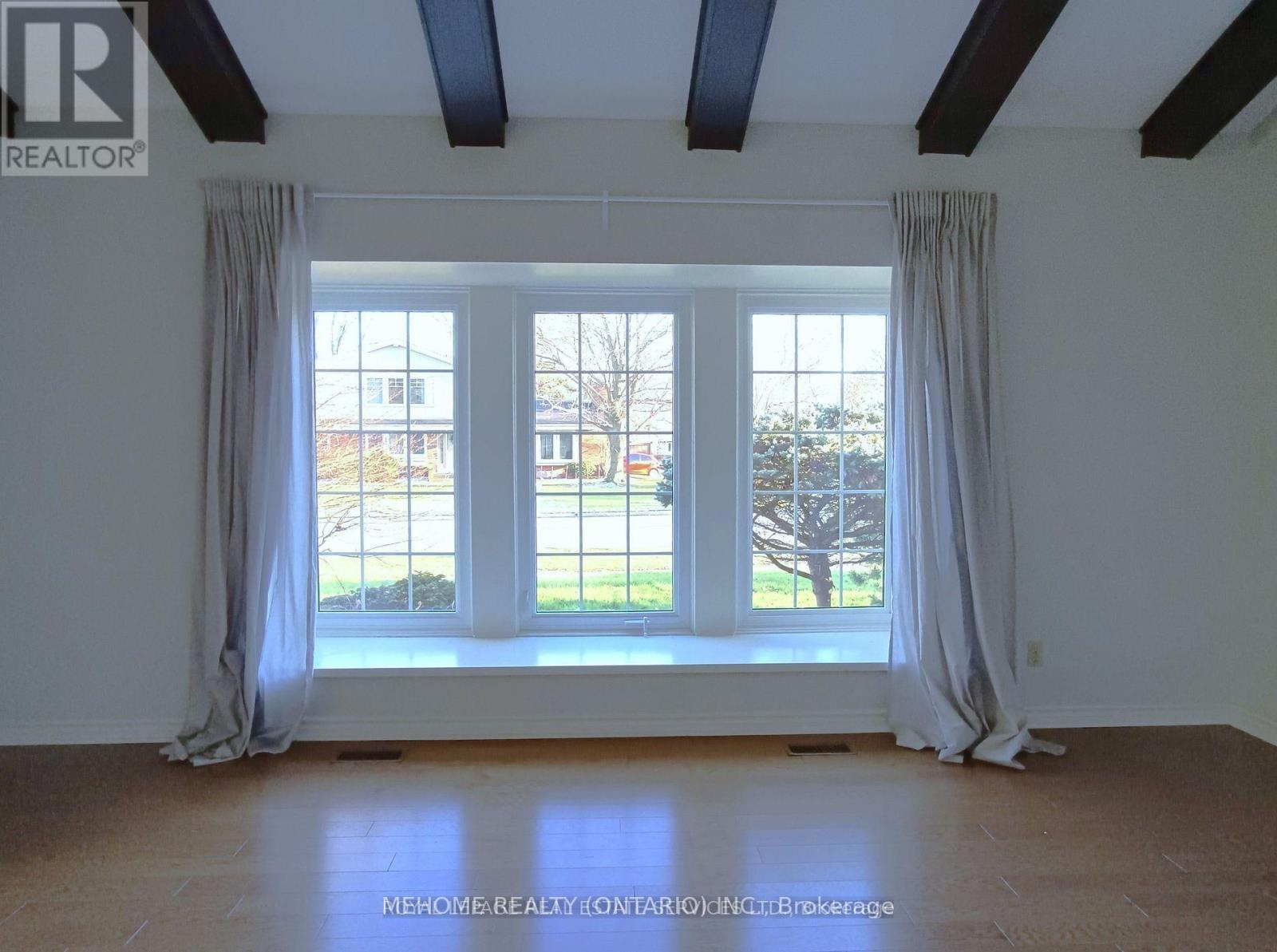 A room with a large window and a view of a tree and a building outside.