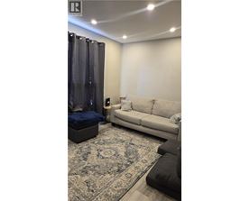 A living room with a grey couch, a blue ottoman, and a patterned rug.