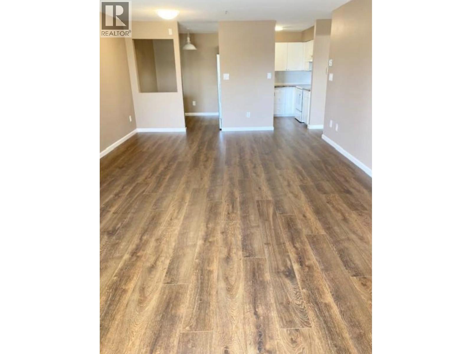 A room with wooden flooring and a Realty logo in the corner.