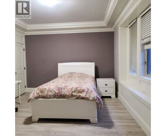 A bedroom with a bed, nightstand, and a window with blinds.