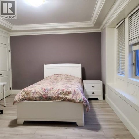 A bedroom with a bed, nightstand, and a window with blinds.