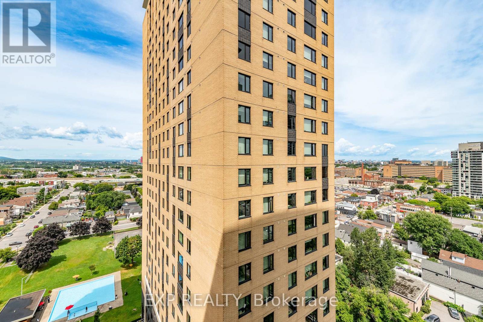 A tall building with a pool in the foreground and a cloudy sky above.