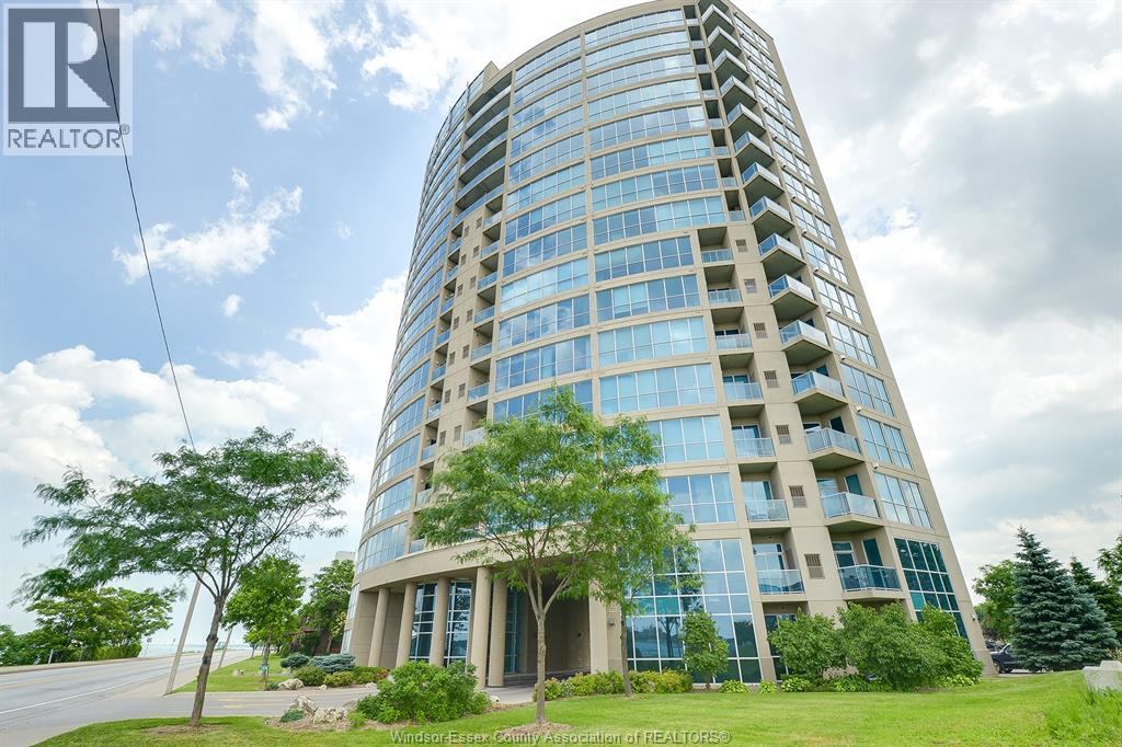 A tall building with many windows and balconies is surrounded by greenery.