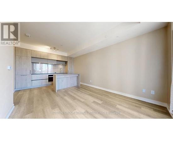 A spacious room with wooden flooring and a kitchen area with a counter and cabinets.