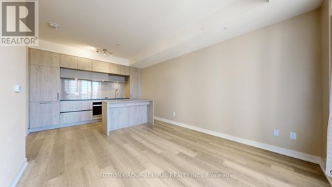 A spacious room with wooden flooring and a kitchen area with a counter and cabinets.