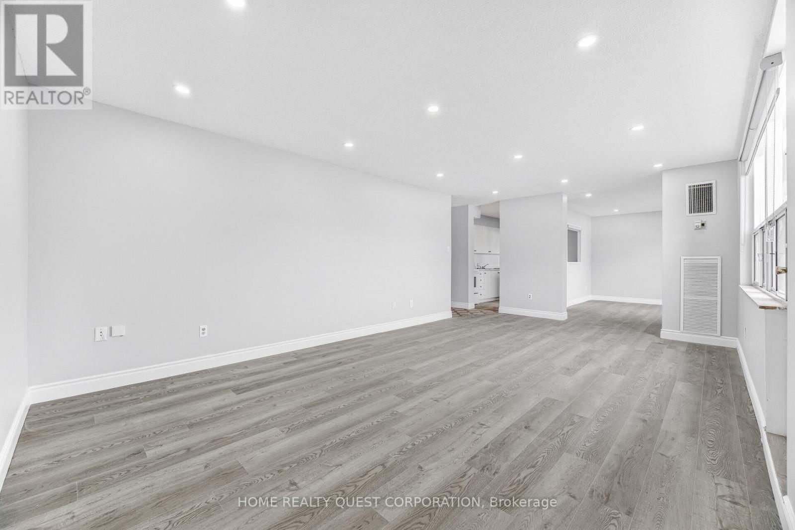A spacious room with wooden flooring and white walls, likely a property for sale.