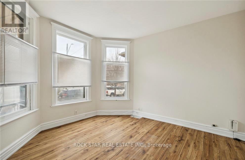 A room with wooden floors and two windows showing a view of a house and trees.
