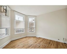 A room with wooden floors and two windows showing a view of a house and trees.