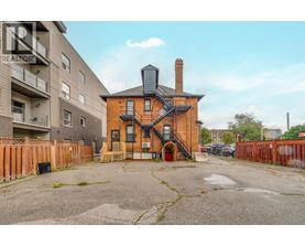 A brick house with a chimney is in the foreground with apartment buildings in the background.