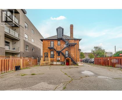 A brick house with a chimney is in the foreground with apartment buildings in the background.