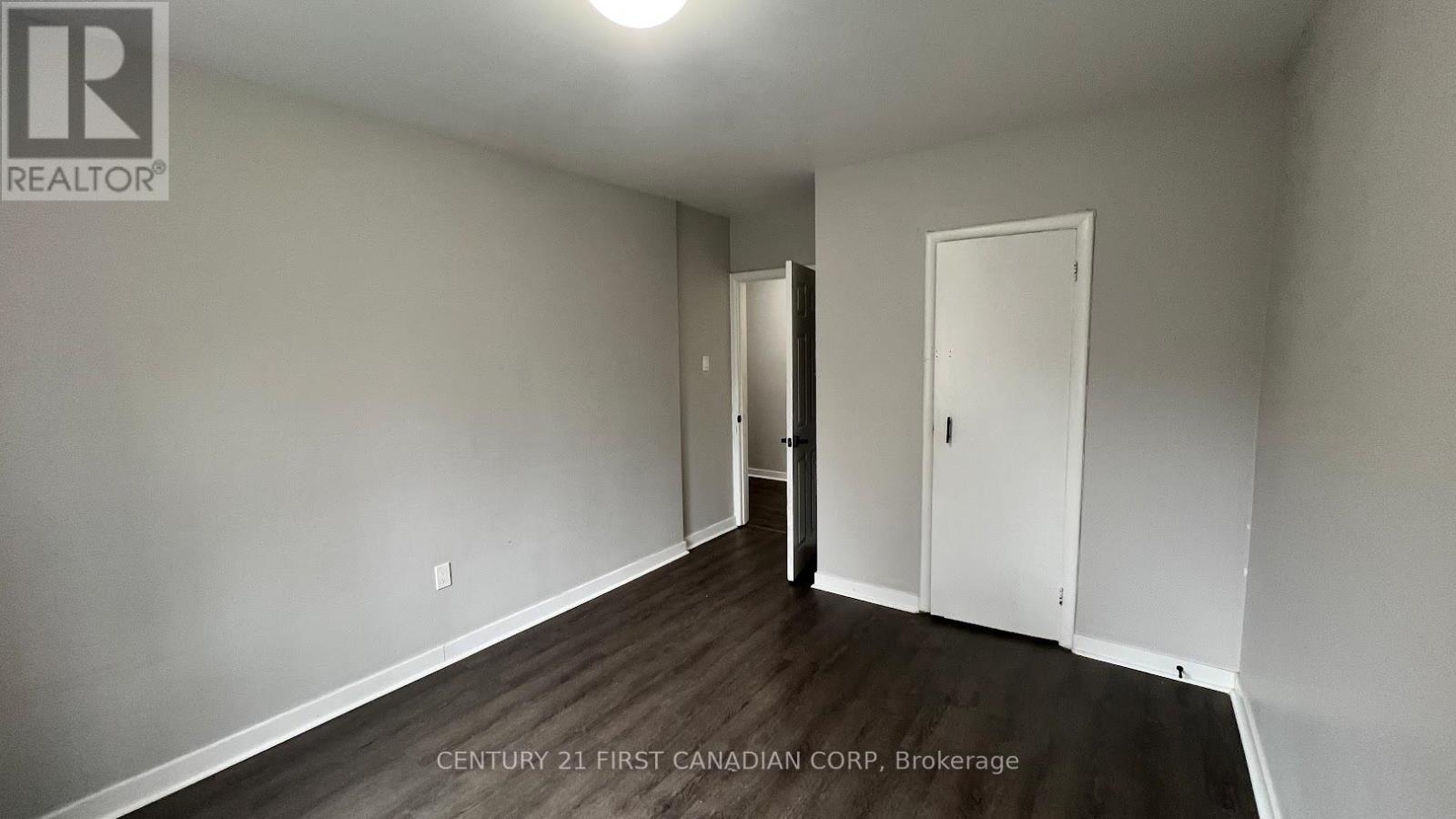 A brokerage sign is on the wall of a white room with wood flooring and a door.