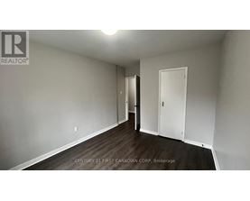 A brokerage sign is on the wall of a white room with wood flooring and a door.