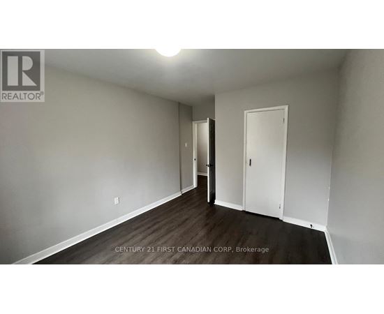 A brokerage sign is on the wall of a white room with wood flooring and a door.