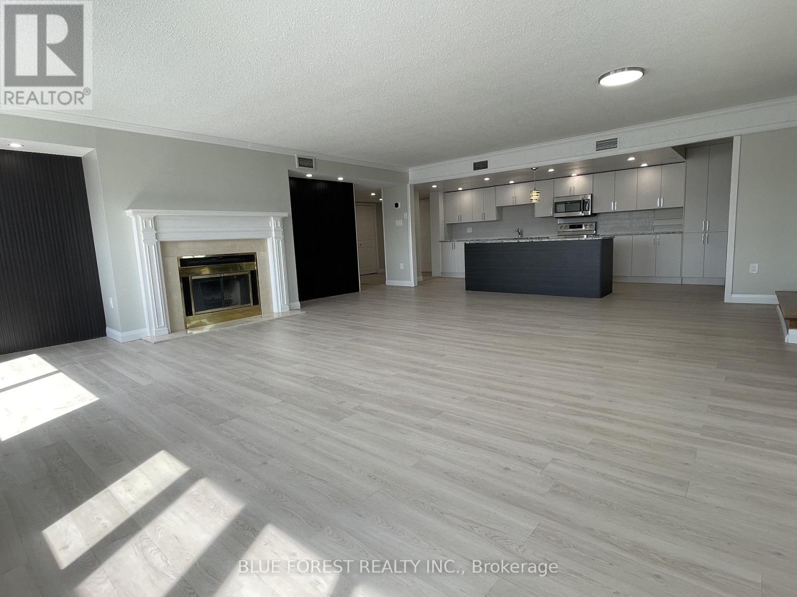 A spacious living room with a fireplace and a kitchen area in the background.