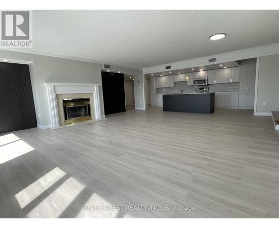 A spacious living room with a fireplace and a kitchen area in the background.