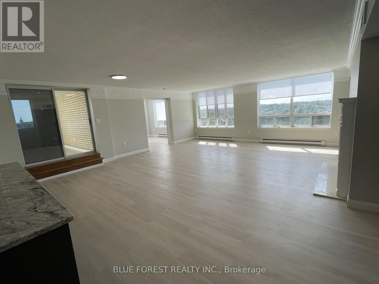 A spacious room with wooden flooring and large windows.