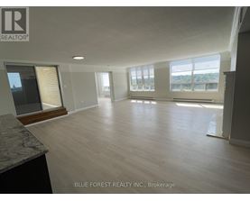 A spacious room with wooden flooring and large windows.