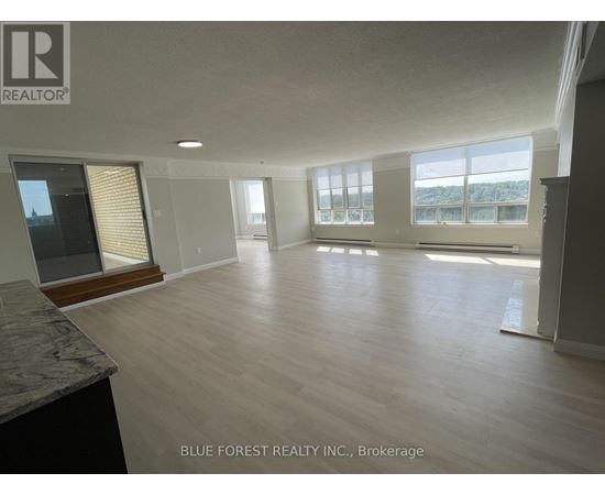 A spacious room with wooden flooring and large windows.
