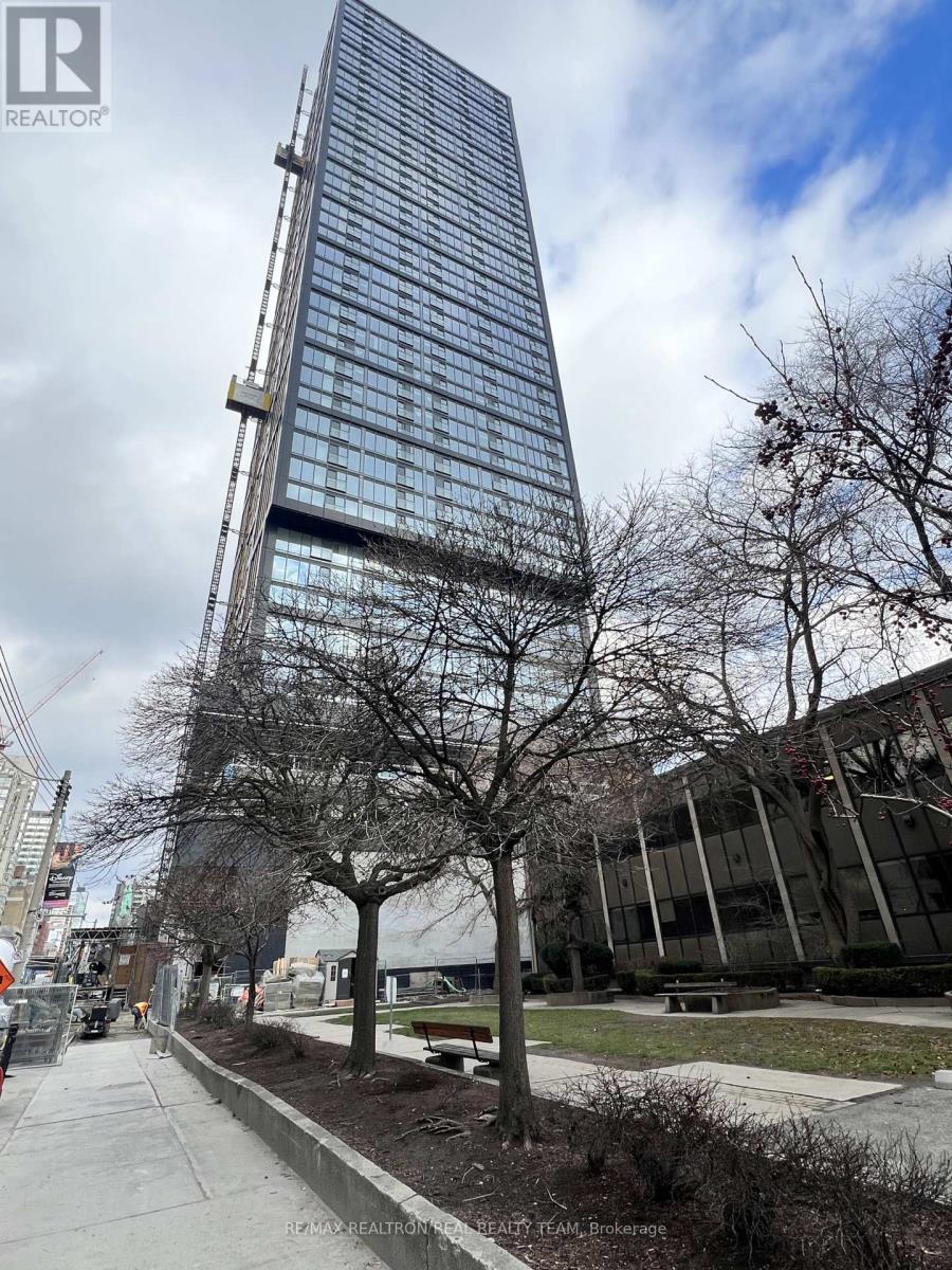A tall building with a glass facade stands next to a sidewalk with bare trees.