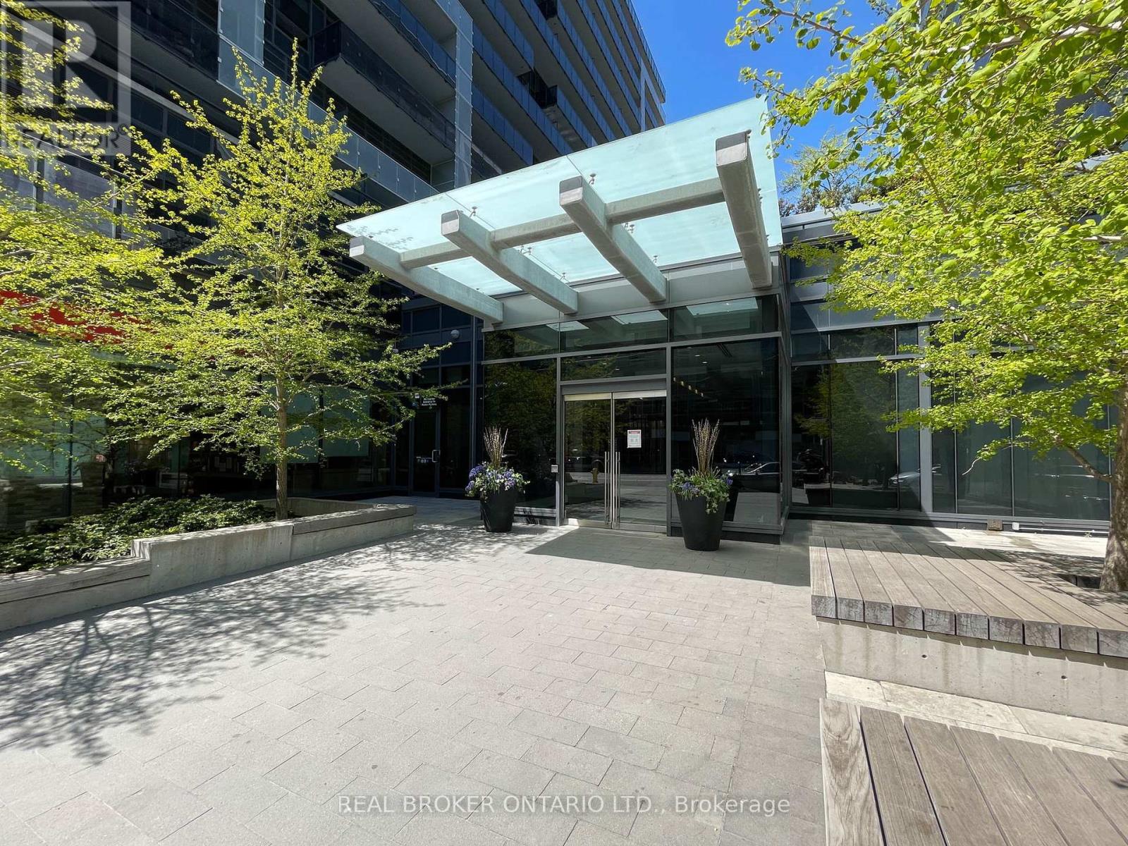 The image shows a modern building entrance with a glass wall and a white awning.