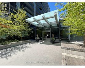 The image shows a modern building entrance with a glass wall and a white awning.