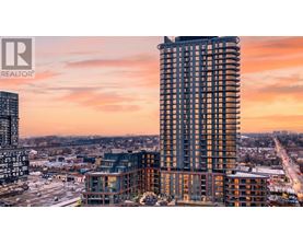 A tall building with a glass facade stands in the foreground of a cityscape at sunset.