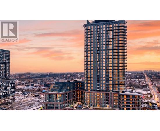 A tall building with a glass facade stands in the foreground of a cityscape at sunset.
