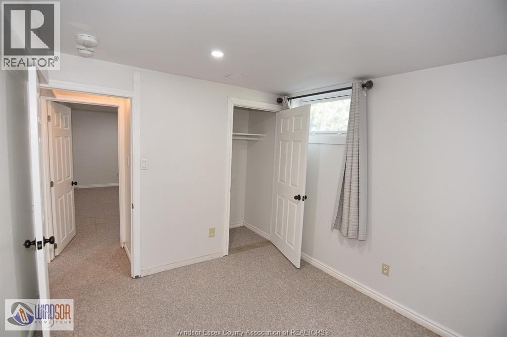 A white bedroom with a carpeted floor and a window with a curtain.