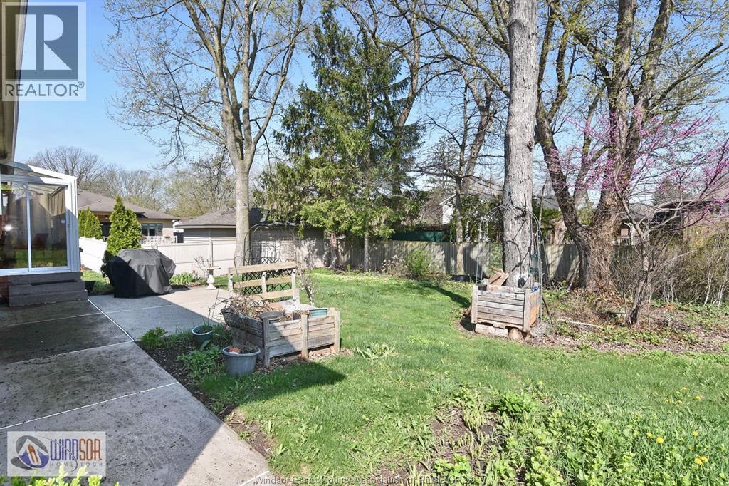 A backyard with a concrete walkway, a wooden bench, and a tree with pink blossoms.