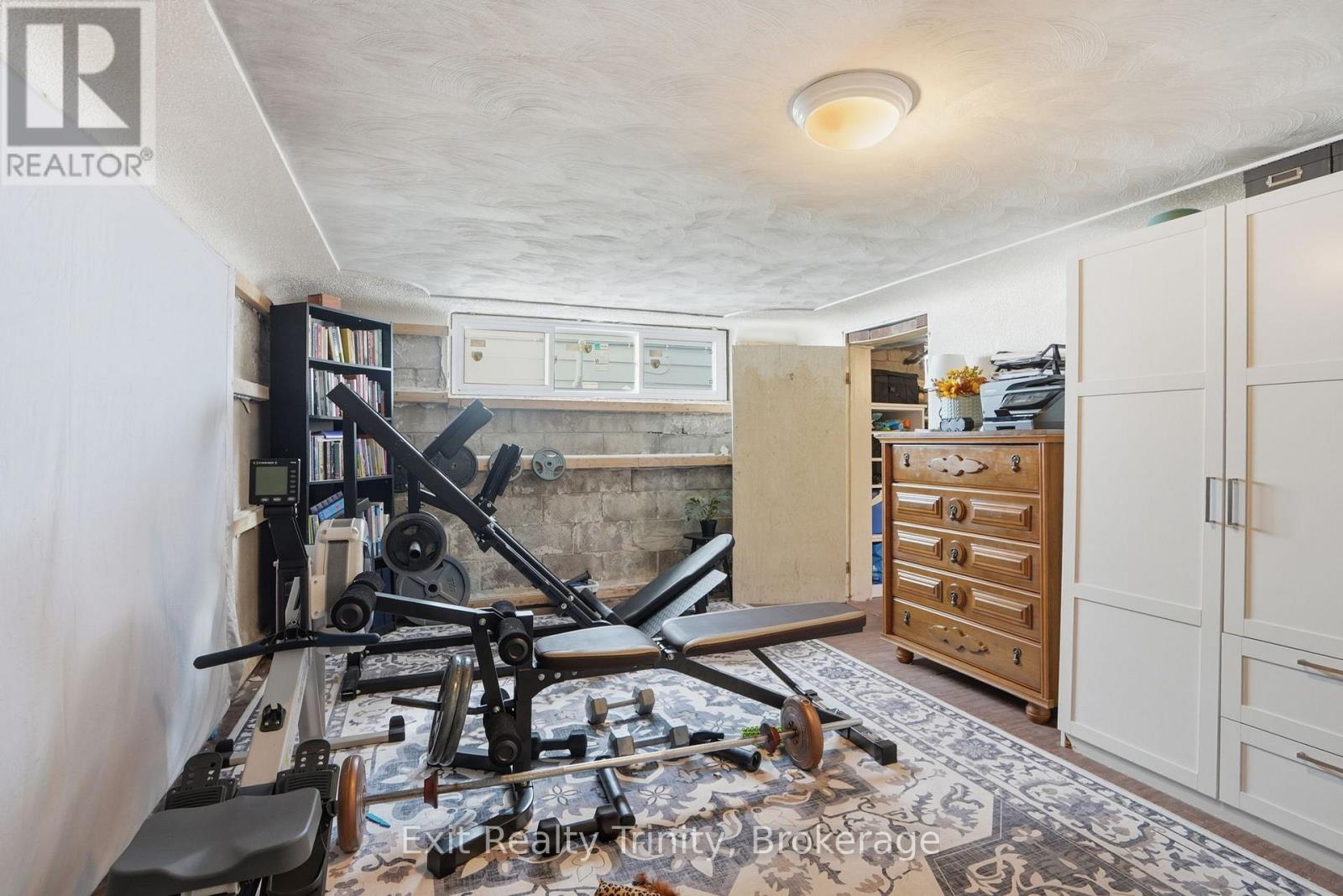 A room with a gym setup and a brokerage logo.