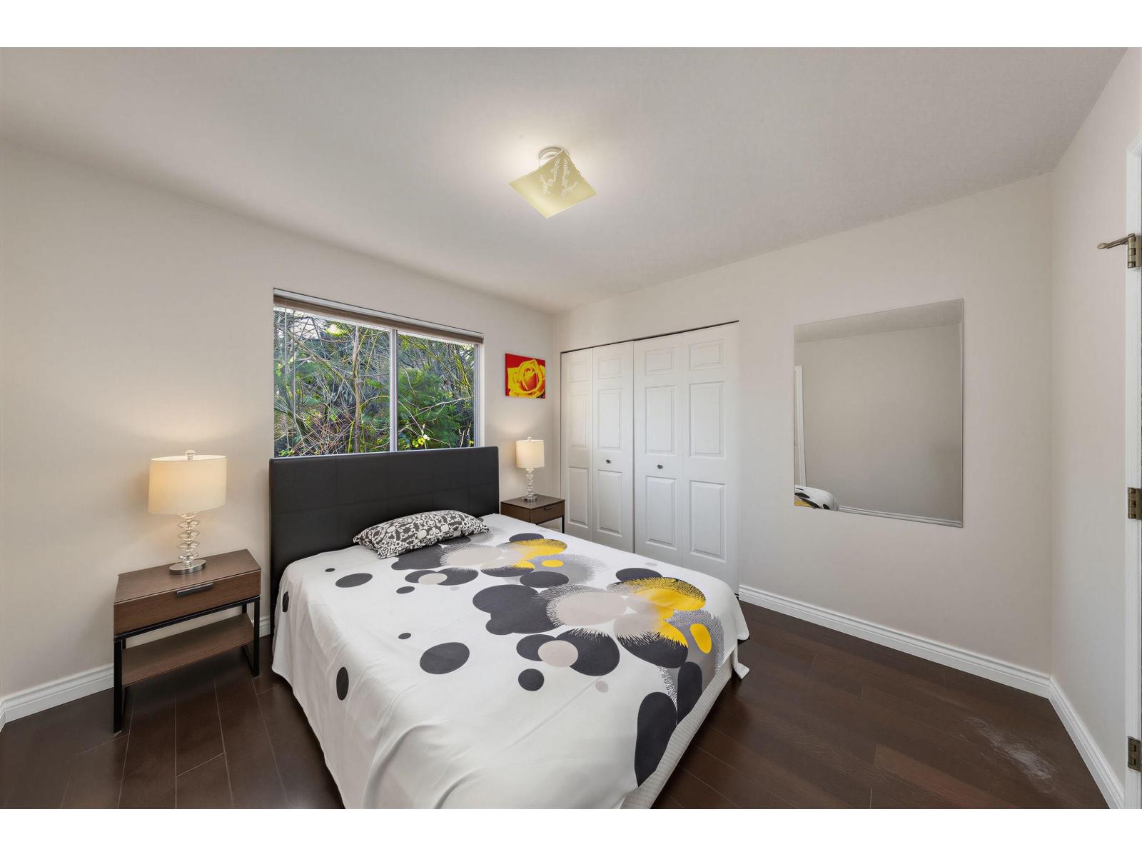 A bedroom with a bed, nightstand, and a window with a view of trees.